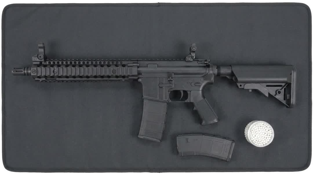 MK18-style AEG airsoft rifle top-down flat-lay on a padded mat with a spare magazine